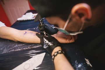 Young focused tattoo artist is inking customers arm carefully in his shop.