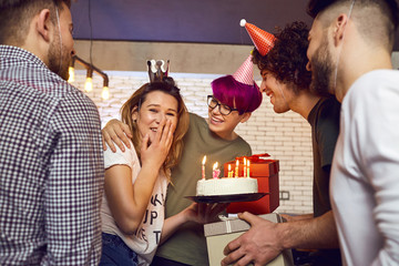 Friends with cake with candles celebrating birthday at a party in room.