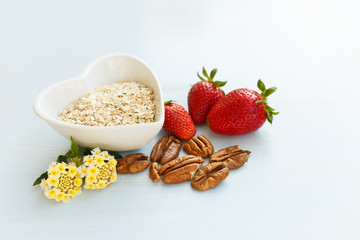 oatmeal in a plate in the shape of a heart, strawberry with a handful of pecans on a blue wooden background with a lantana flower at breakfast