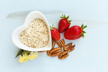 oatmeal in a plate in the shape of a heart, strawberry with a handful of pecans on a blue wooden background with a lantana flower at breakfast