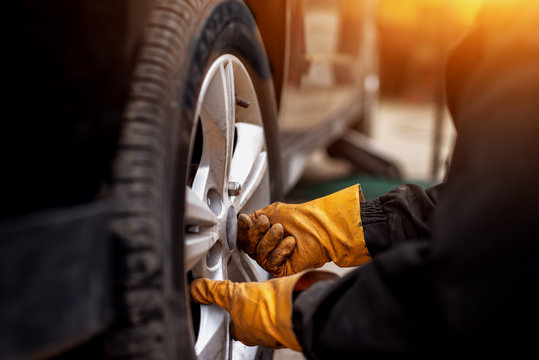 An Experienced Mechanic With Orange Gloves Is Putting Screws On A Placed Wheel On A Car.