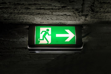 emergency exit light green sign on brick ceiling in the dark