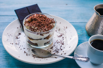 Homemade Italian dessert tiramisu in a glass with grated chocolate, and a cup of coffee on a rustic table