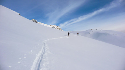 two backcountry skiers on a tour in the Austrian Alps and putting in new tracks on their way to the summit
