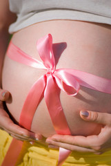 Closeup view of pregnant woman hugging her round big belly with both hands. Vertical color photography.