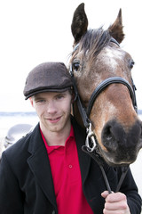 Fototapeta premium Portrait of horse rider and brown horse. He is wearing a flatcap, red polo shirt and black jacket 