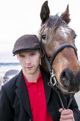 Portrait of  horse rider and brown horse. He is wearing a flatcap, red polo shirt and black jacket 