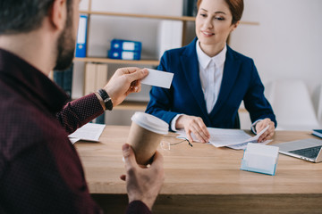 partial view of client with blank card and businesswoman at workplace in office