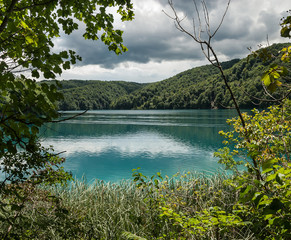 A fantastic landscape of an azure lake, surrounded by green hills, opening through branches of the trees, Croatia.