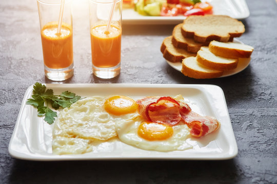 Daily Breakfast. Fried egg with bacon, carrot juice, vegetable salad, bread. On dark stone background