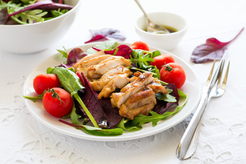 Sliced grilled chicken with green leaves salad on white plate