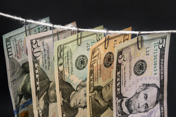 Different new dollar bills are hanging on clerical clips on a rope on the dark background. Closeup,...