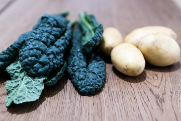 Black cabbage leaves with potatoes on a wooden table. Organic and winter food ready to be cooked, choice of healthy food and oriented to low environmental impact