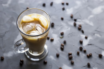 Black cold coffee with ice and milk on a gray background among the coffee beans. Summer cooling drink in a glass cup