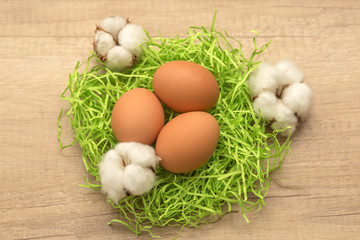 raw chicken eggs and cotton inflorescences on a wooden background
