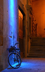 cruiser bike leaning against a wall, in a corner of the historical site of arezzo (tuscany/Italy), lluminated by artificial and suffused blue/orange lights 