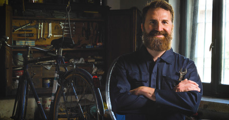 Well-groomed handsome bearded master hipster, specialist in bicycles, repairing a bicycle in his...
