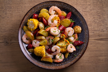 Shrimp boil. Shrimps, smoked sausages, potatoes and corn in bowl on wooden table. overhead, horizontal