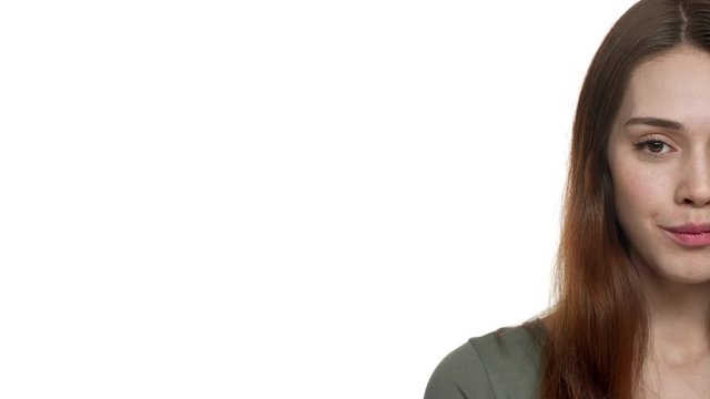 Half side portrait of young pretty woman 20s ooking on camera and smiling near copyspace, isolated over white background in studio. Concept of emotions