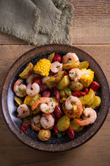 Shrimp boil. Shrimps, smoked sausages, potatoes and corn in bowl on wooden table. overhead, vertical