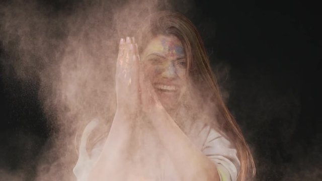Portrait of delighted woman making splash with colorful powder and celebrating holi spring festival of colors, isolated over dark gray background slow motion. Indian culture and tradition