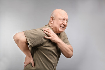 Senior man suffering from pain in shoulder on light background