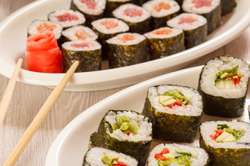 Sushi rolls with nori, rice, pieces of avocado, cucumber, red bell pepper and lettuce leaves on ceramic plate