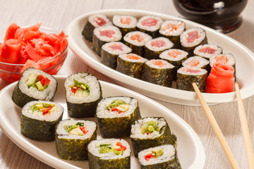 Different  sushi rolls on ceramic plate, chopsticks, glass bottle with soy sauce and pickled ginger in a bowl