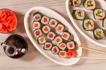 Fototapeta na wymiar Different sushi rolls on ceramic plate, chopsticks, glass bottle with soy sauce and pickled ginger in a bowl
