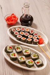 Different  sushi rolls on ceramic plate, chopsticks, glass bottle with soy sauce and pickled ginger in a bowl