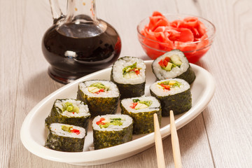 Sushi rolls with rice on ceramic plate, chopsticks, glass bottle with soy sauce and pickled ginger in a bowl