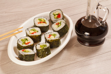 Sushi rolls with rice, pieces of avocado, cucumber and lettuce leaves on ceramic plate, glass bottle with soy sauce