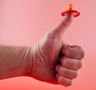 hand and a red condom on a pink background