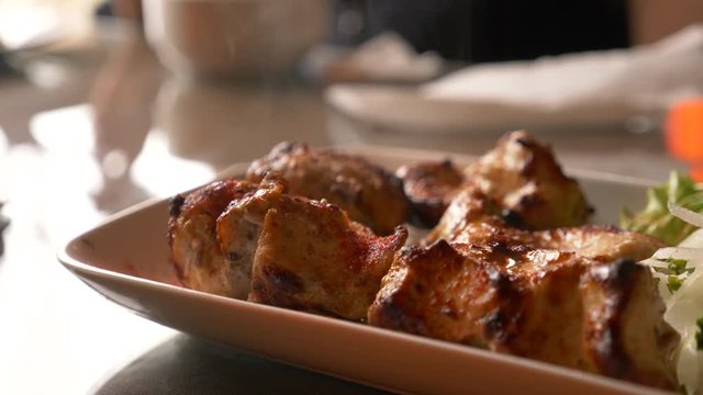 Close of roasted meat lying on a white plate with greens on a table in slow motion, 4k, steam from hot meat