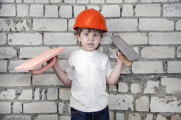 boy in a construction worker's helmet with tools for putty on a white brick wall background