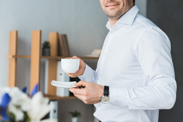 Close-up view of businessman holding cup with coffee in office