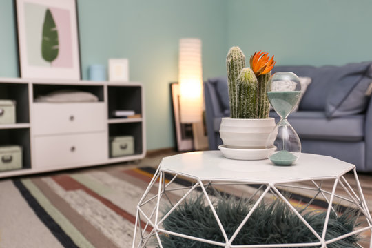 Stylish table with hourglass and cactus in living room