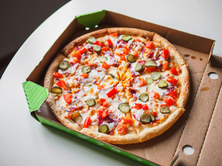 Cheeseburger pizza in delivery cardboard box on white table