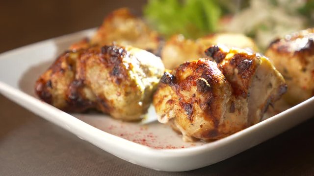 Close of roasted meat lying on a white plate with greens on a table in slow motion, 4k, steam from hot meat