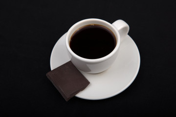 White cup of coffee with chocolate  on black surface