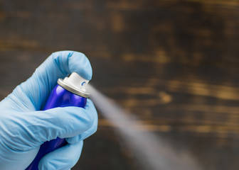Spray the aerosol from the can with a hand in a rubber glove against a dark background.