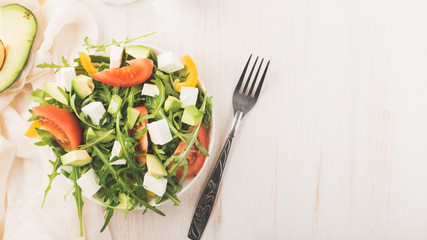 Salad in bowl on a wooden table. Fresh green arugula, feta cheese, paprika, tomatoes. Bottle of olive oil. Diet, healthy eating and weigh loss concept