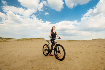 Bicyclist at the summer sunset on the desert road in the reserve territory. Full length image of young female cyclist. Summer sunset. Bicycle and ecology lifestyle concept.