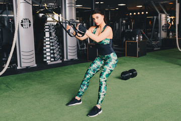 TRX concept. Beautiful lady exercising her muscles with help of suspension trainer sling or...