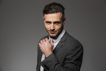 Photo closeup of businesslike man wearing formal suit looking on camera with confident gaze, isolated over gray background