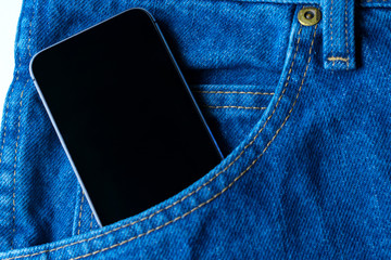 Black modern smartphone in the pocket of old vintage indigo stonewashed jeans. Concept of daily things of modern man. Trendy color