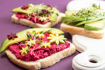 Healthy breakfast toasts with feta, beetroot, slices of avocado and microgreen. Clean eating vegan dieting concept. Trend color ultraviolet background. Top view.