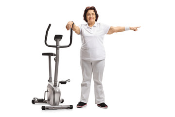 Elderly woman leaning on an exercise bike and pointing