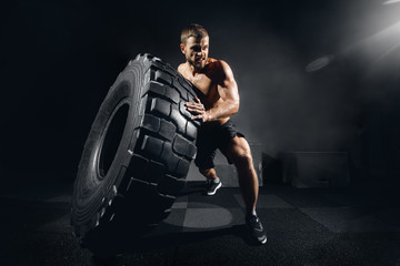 Muscular fitness shirtless man moving large tire in gym fitness center, concept lifting, workout...