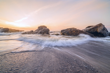 A beautiful dawn on the beach. The wave is approaching the shore. Waves breaking against stones. Long exposure
